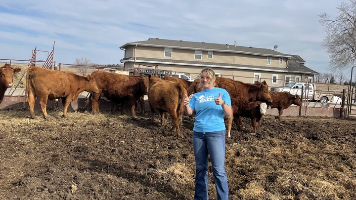 Chaylee Tonninges in a feed lot in front of cattle.