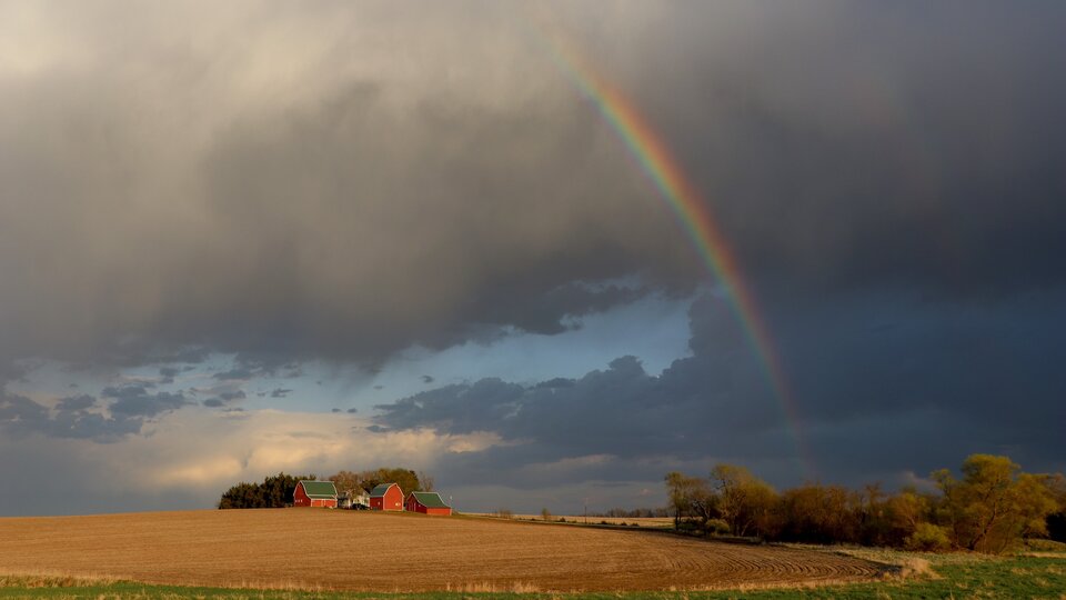 A farmstead below dark clouds and a rainbow.